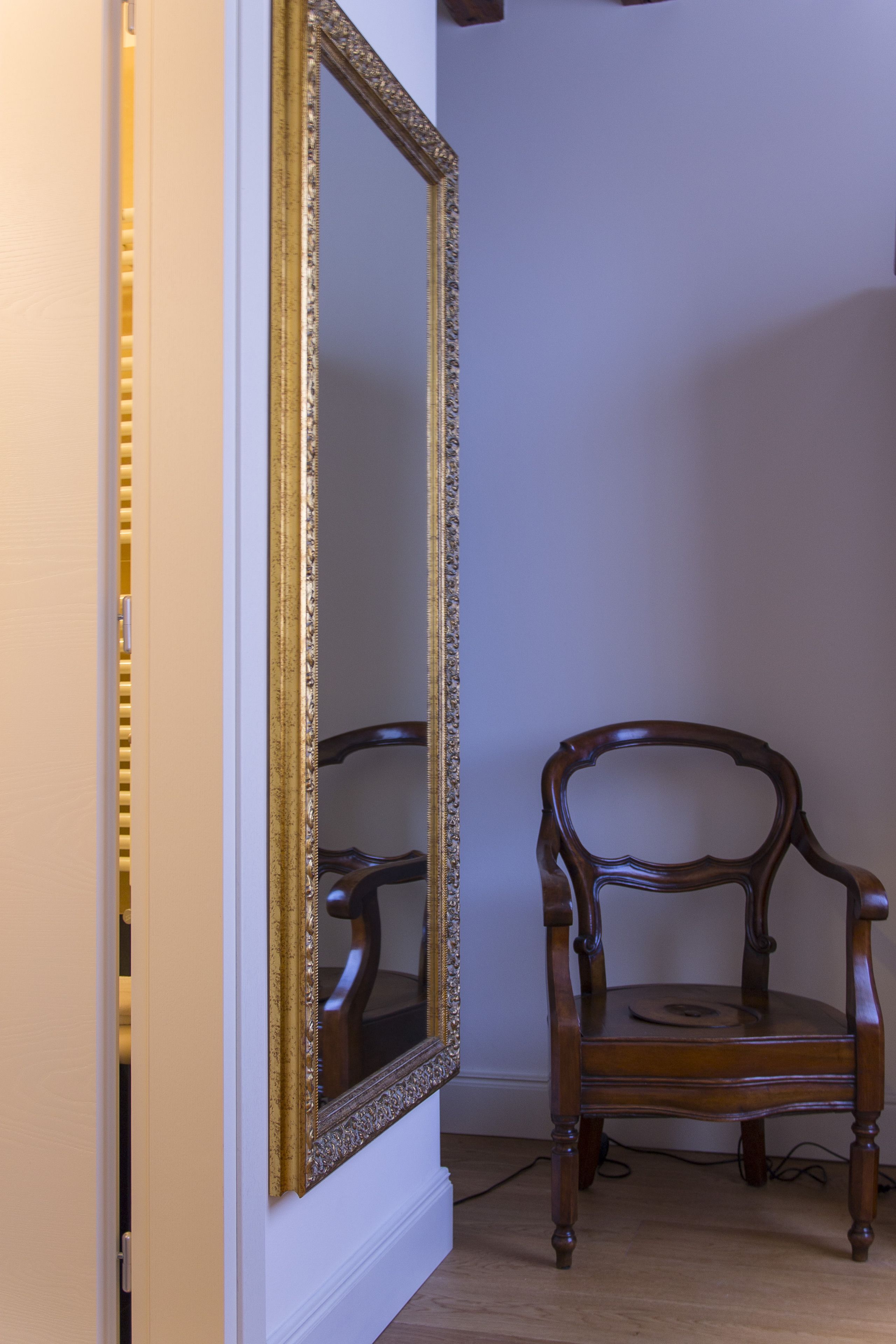 Una stanza con uno specchio grande e decorato e una sedia di legno.
