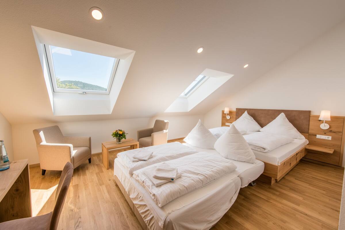 A modern bedroom with a skylight, a bed with white linens, a wooden nightstand, and a chair.