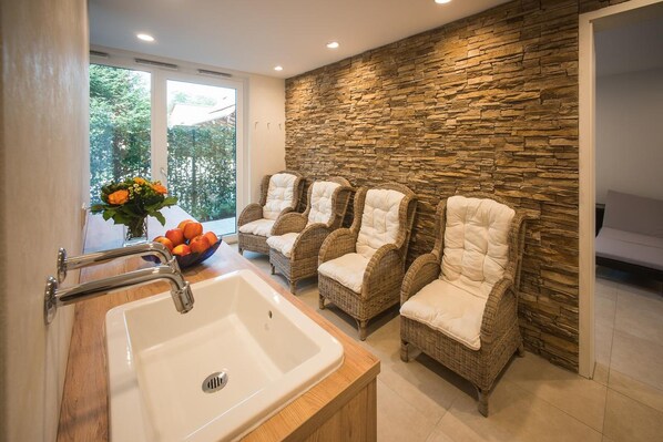A bathroom with a stone wall, a sink, and three wicker chairs with white cushions. - Hotel & Gasthaus Löwen (Waldkirch)