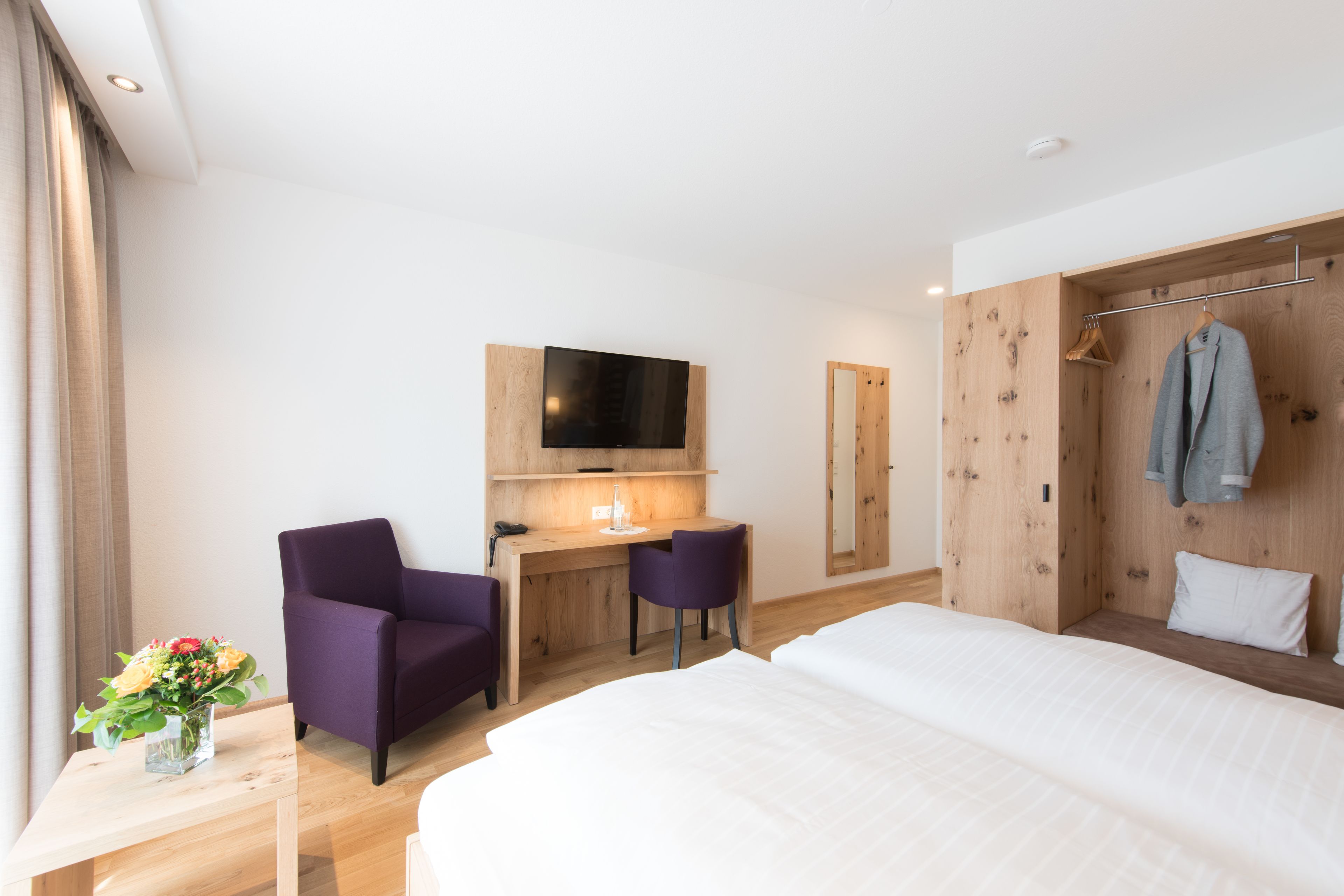 Una habitación de hotel con una cama, un escritorio con dos sillas, un televisor y un armario.