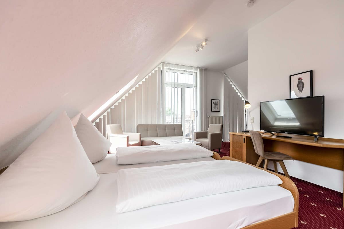 A hotel room with a bed, a desk with a TV, a chair, and a sofa.
