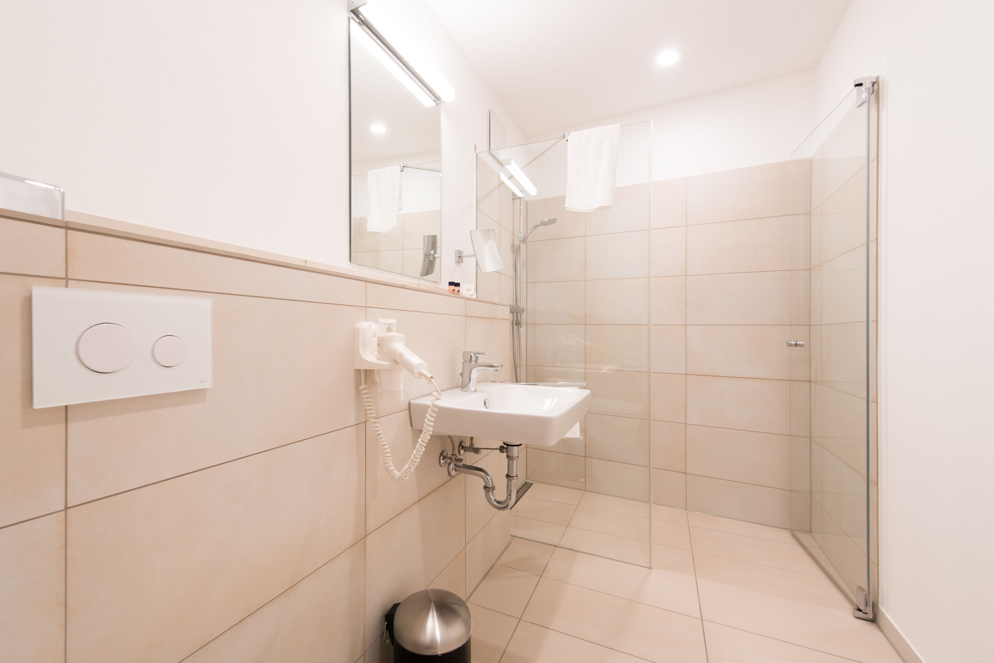 A modern bathroom with a glass shower enclosure, a white sink, and a hairdryer mounted on the wall.