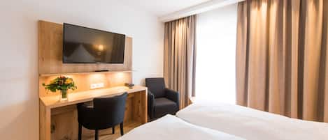 A hotel room with a wooden desk, a flat-screen TV, a black chair, and a bed with white linens.