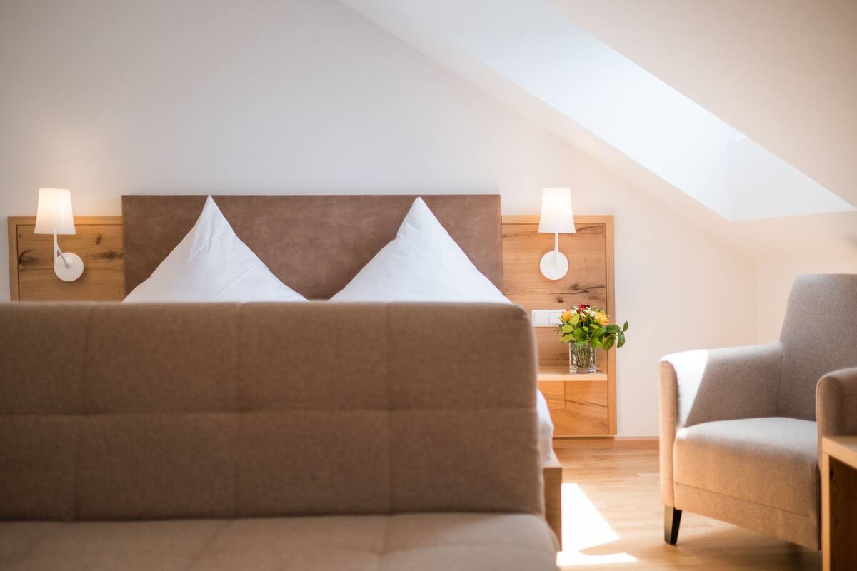 A bedroom with a bed, two bedside lamps, a nightstand with a vase of flowers, and a chair.