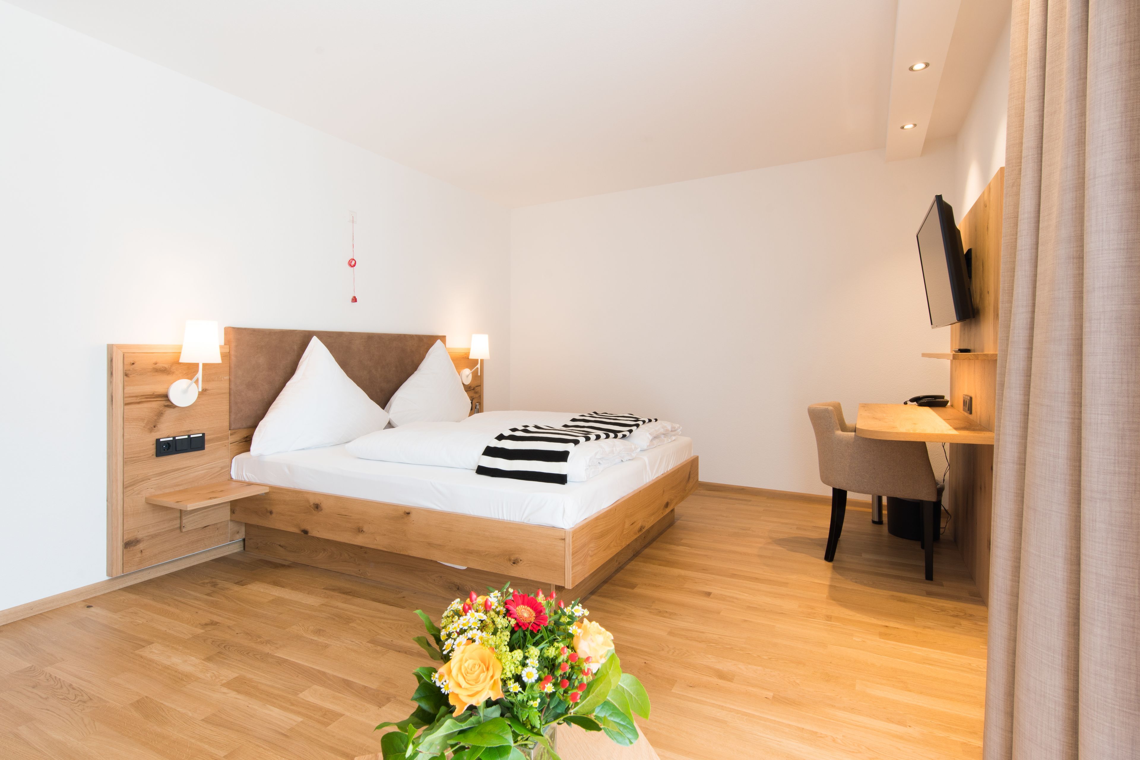 Un dormitorio moderno con una cama de madera, mesitas de noche, un escritorio y un televisor.