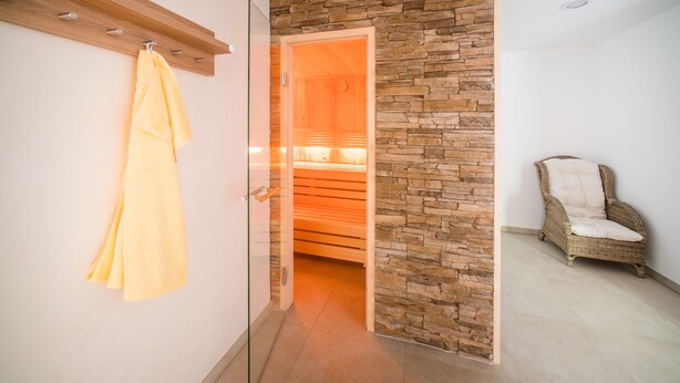 A room with a glass door leading to a sauna area, a wicker chair, and a towel hanging on the wall. - Hotel & Gasthaus Löwen (Waldkirch)