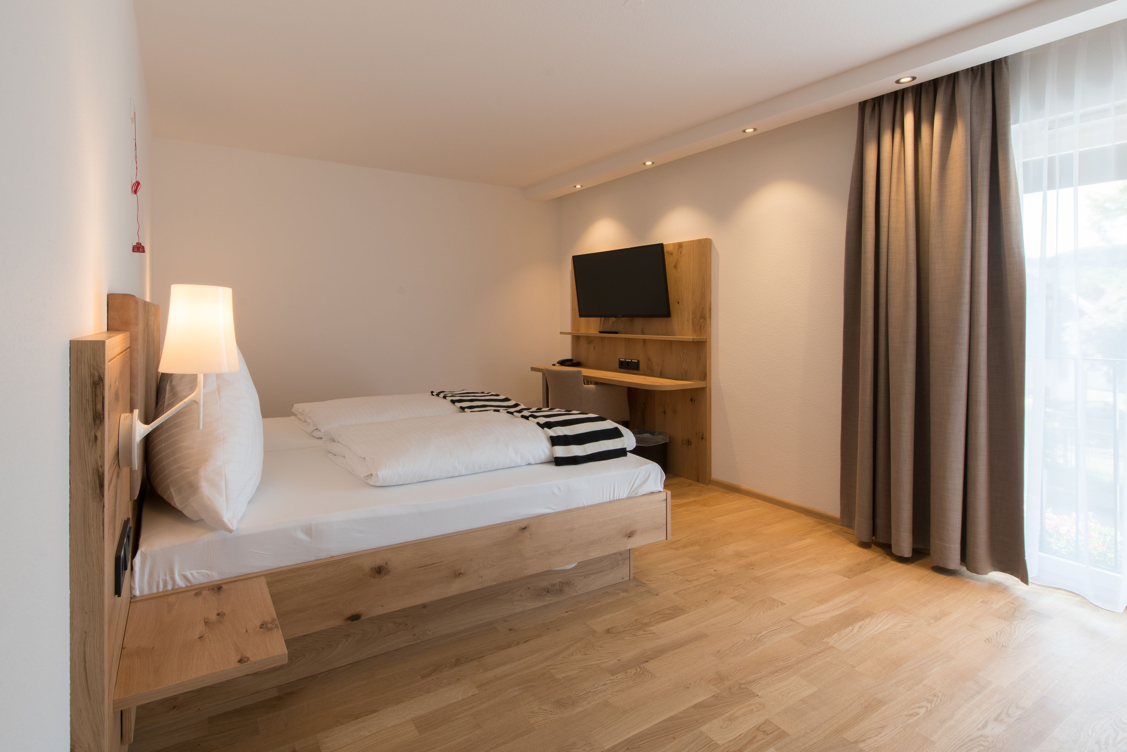 Een moderne slaapkamer met een houten bed, een wandgemonteerde televisie en een groot raam met gordijnen.