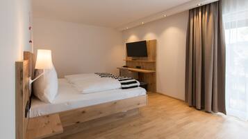 Een moderne slaapkamer met een houten bed, een wandgemonteerde televisie en een groot raam met gordijnen.