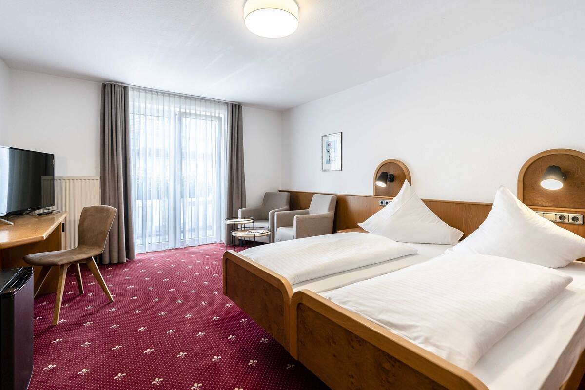 A hotel room with a bed, a desk, a chair, and a television.