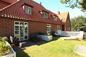 A red brick house with a sloped roof, large windows, and a white porch with wicker furniture.