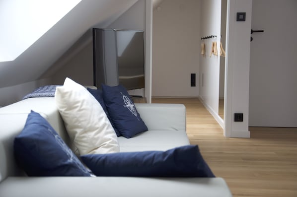 Una sala de estar moderna con un sofá blanco, cojines azules y blancos, y un televisor.