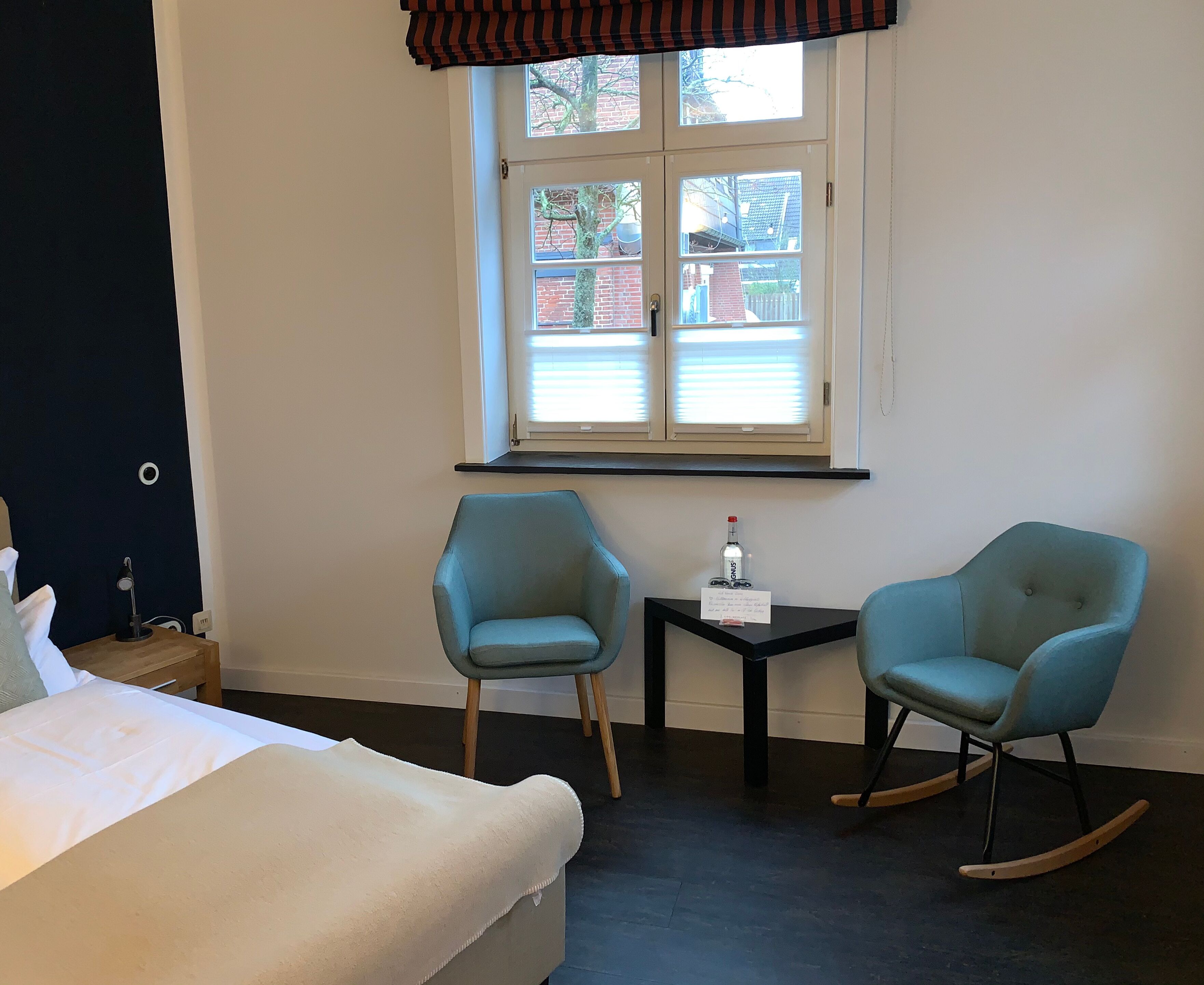 A hotel room with a bed, two chairs, a small table, and a window with blinds.