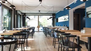 A modern restaurant with long wooden tables and black chairs, large windows, and blue walls. - Lieblingsplatz Strandhotel (St. Peter-Ording)