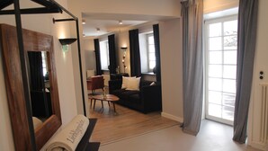 A hotel room with a wooden floor, a black sofa, a small round table, and a large window with curtains. - Lieblingsplatz Strandhotel (St. Peter-Ording)