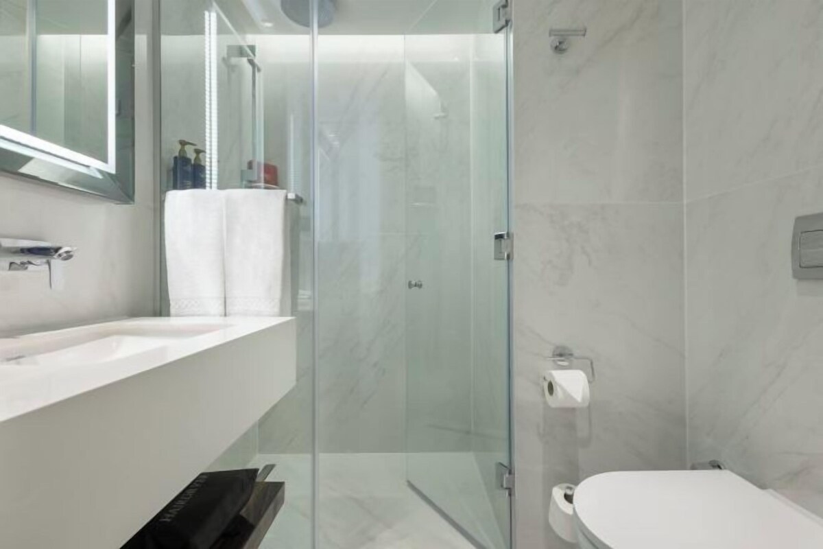 A modern bathroom with a glass-enclosed shower, a white sink, and a toilet.