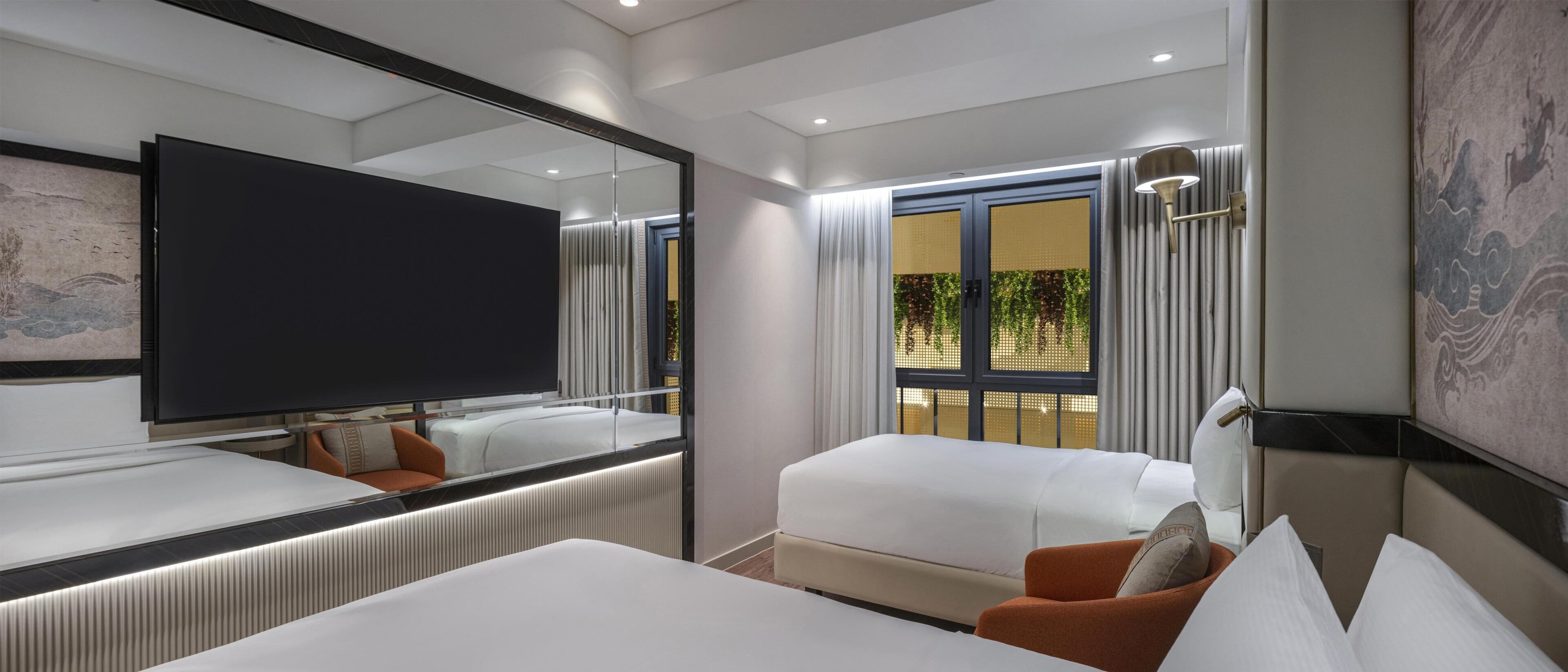 A modern hotel room with a large flat-screen TV, a bed, a sofa, and a large mirror.