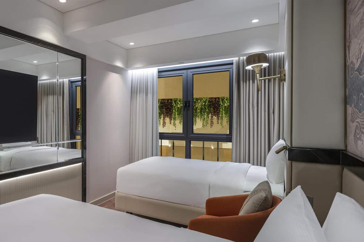 Una habitación de hotel moderna con una televisión de pantalla plana grande, una cama, un sofá y un espejo amplio.