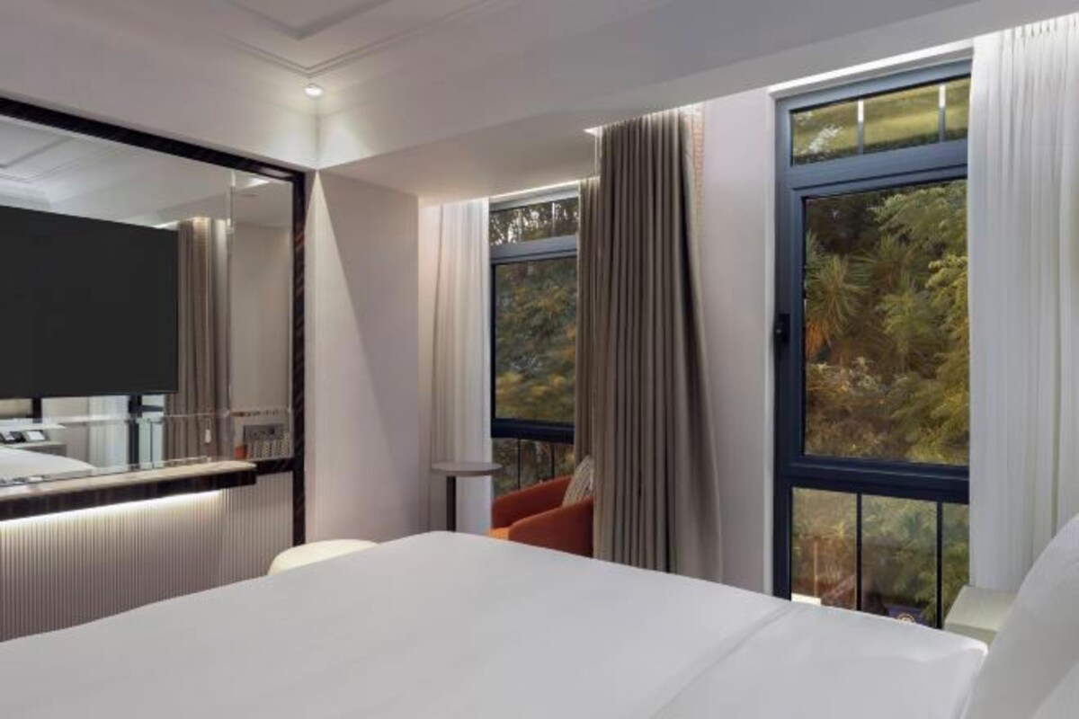 A modern hotel room with a large bed, a bedside table, a mirror, and a window with curtains.