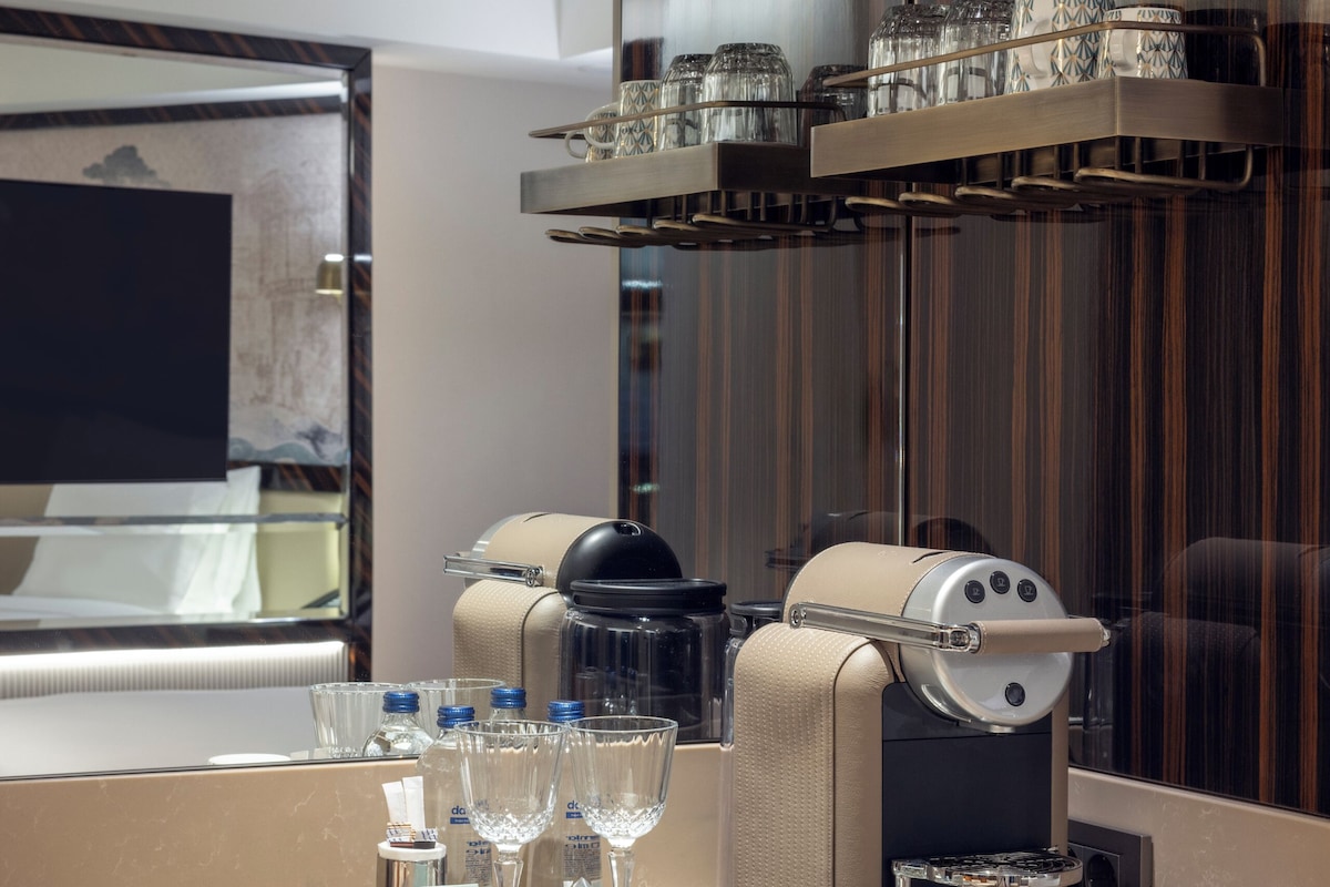A modern hotel room with a minibar, a coffee machine, and a tray with glasses and toiletries.