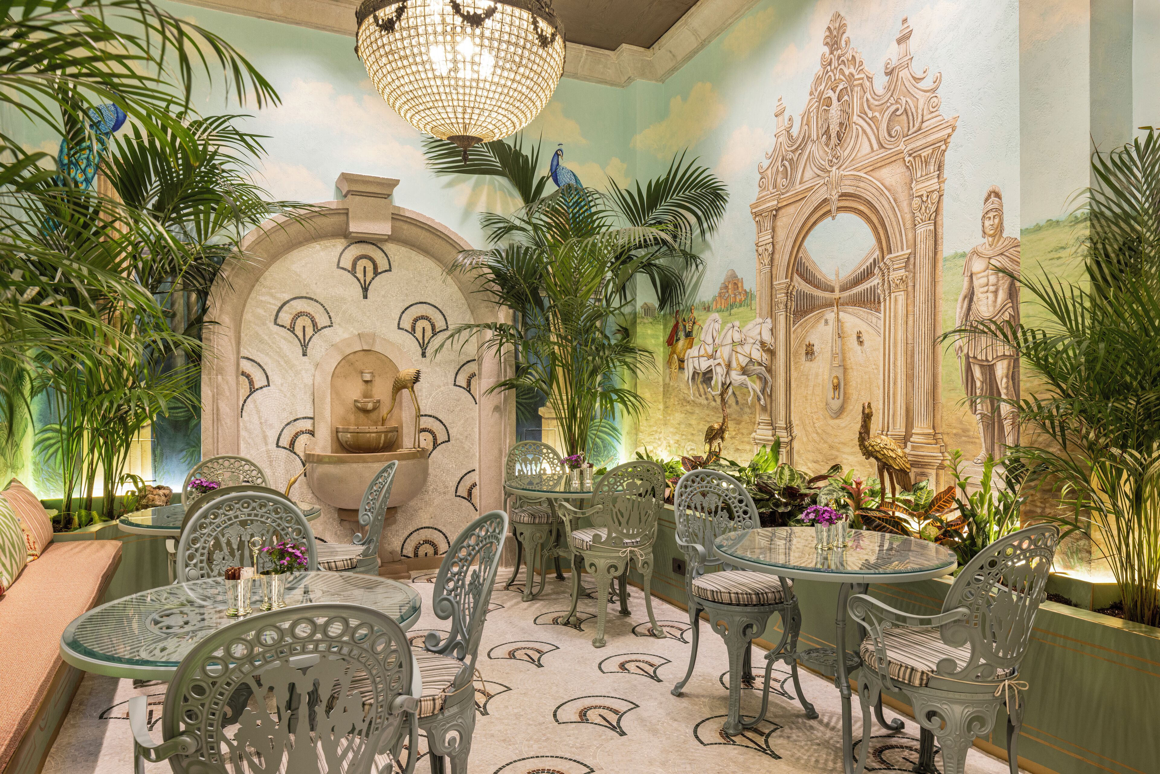 A dining area with ornate chairs, a glass table, and a mural of a historical building.