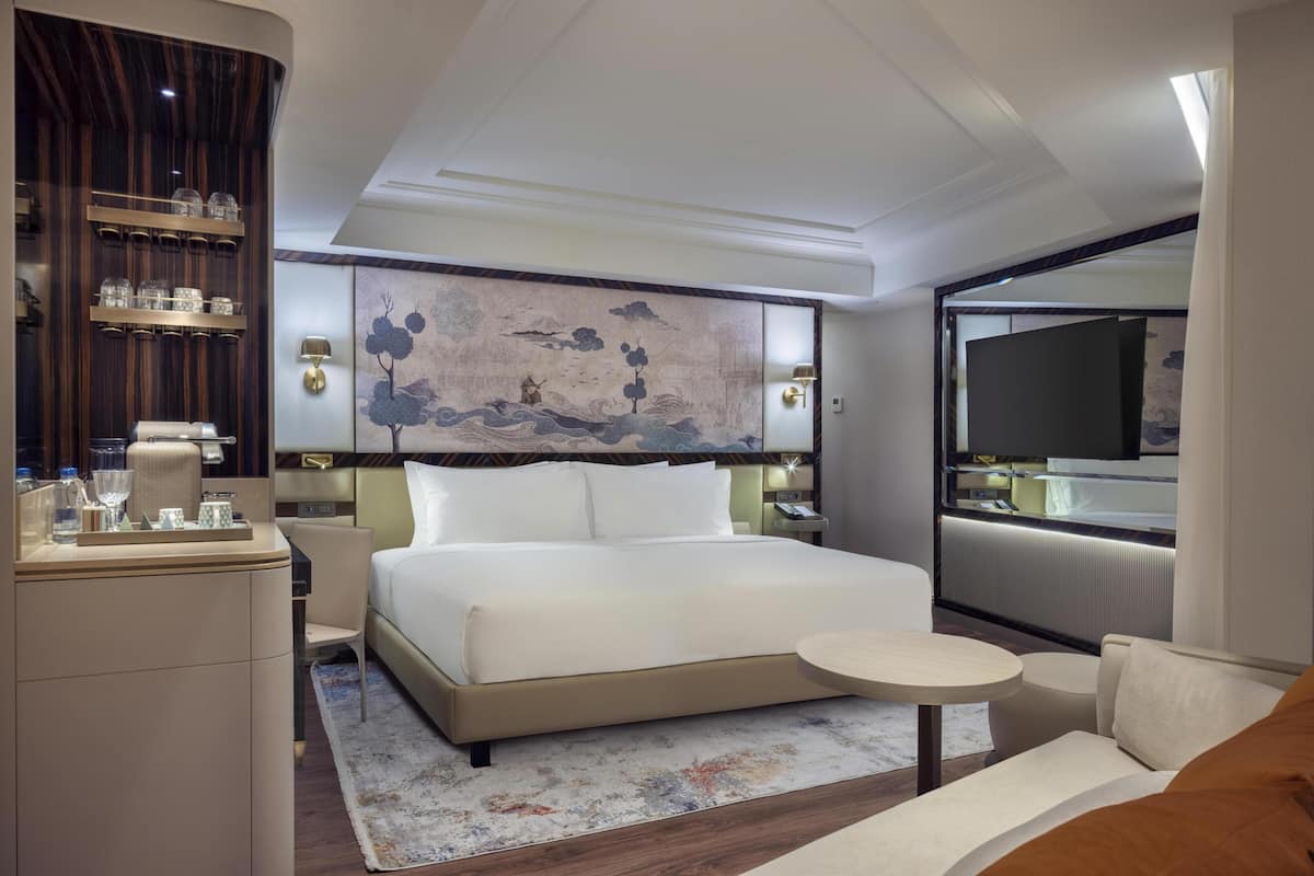 Una habitación de hotel moderna con una cama grande, mesitas de noche, una pequeña mesa redonda y un televisor fijado a la pared.