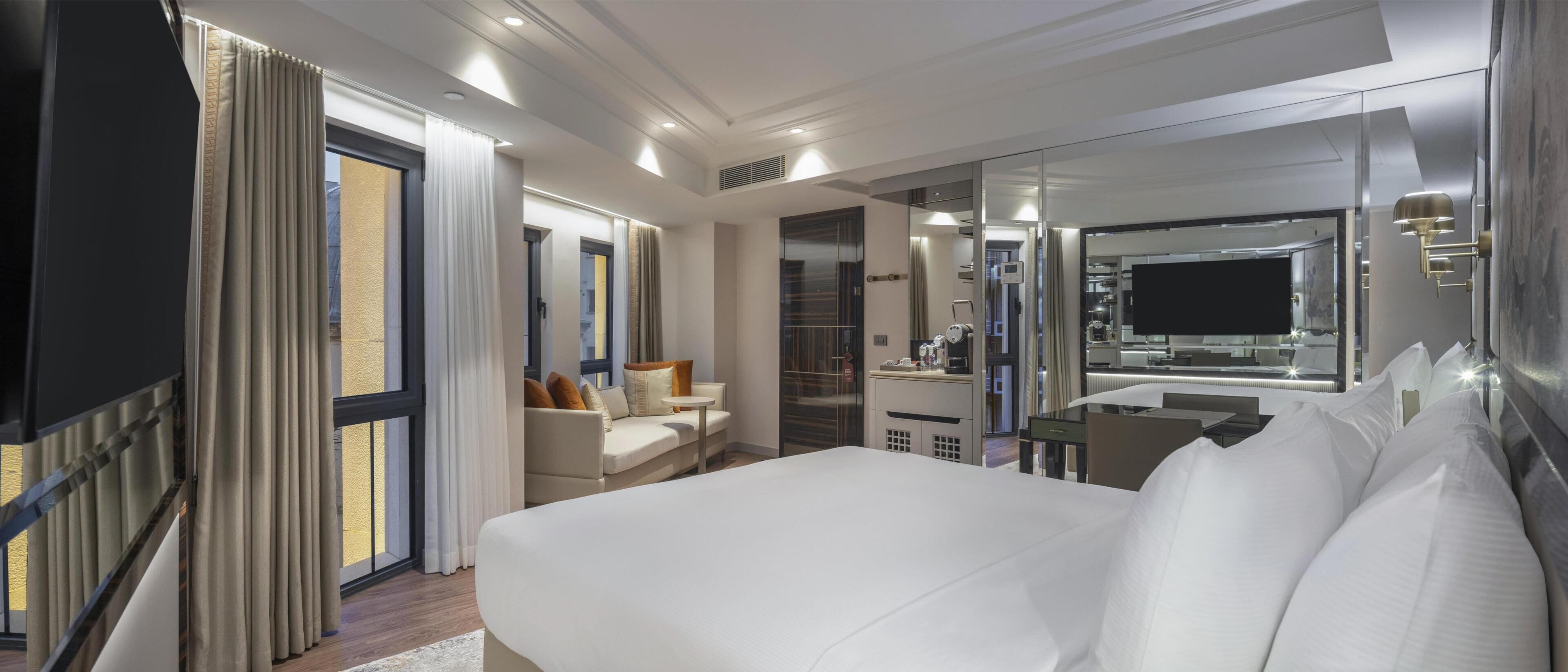 A hotel room with a bed, a sofa, a desk, and a mirror.
