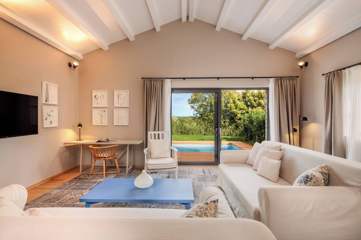 A modern living room with a large window, a white sofa, a blue coffee table, and a white armchair.