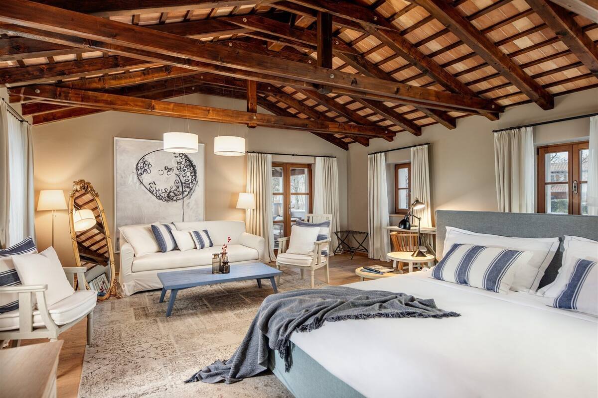 A room with a bed, a sofa, a chair, a table, and a lamp.