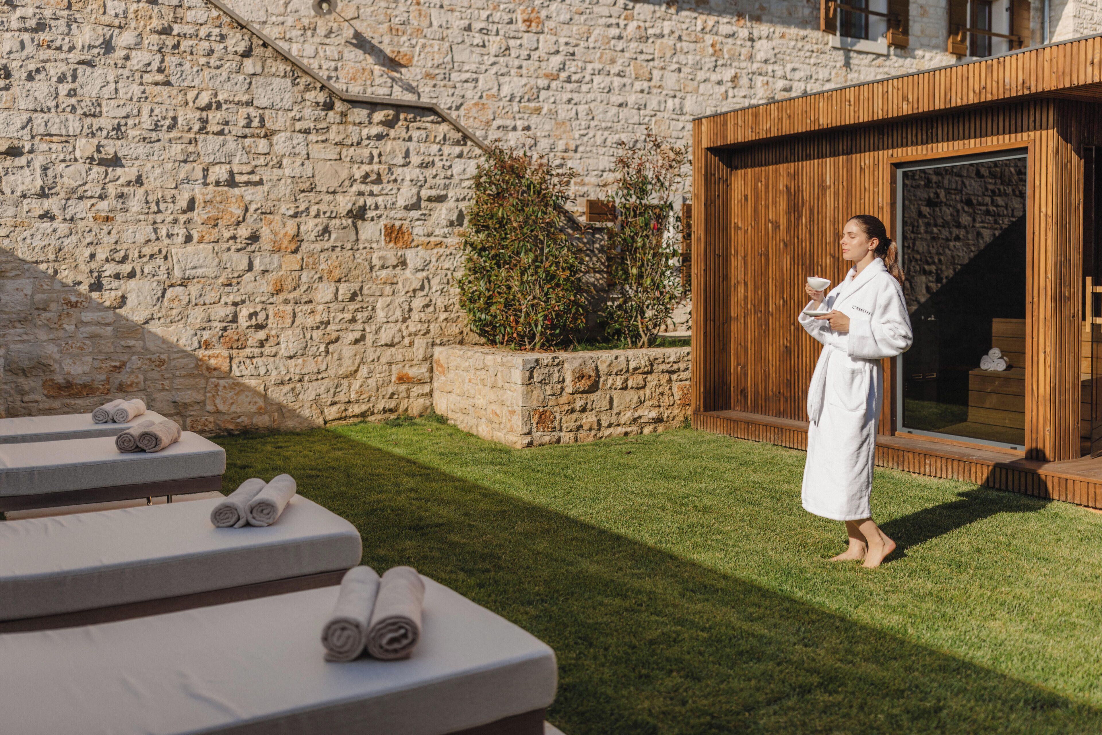 A stone wall, a wooden structure, and a person in a robe holding a cup.
