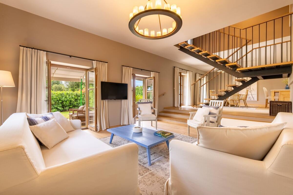 A spacious living room with a large sofa set, a coffee table, and a staircase leading to an upper level.