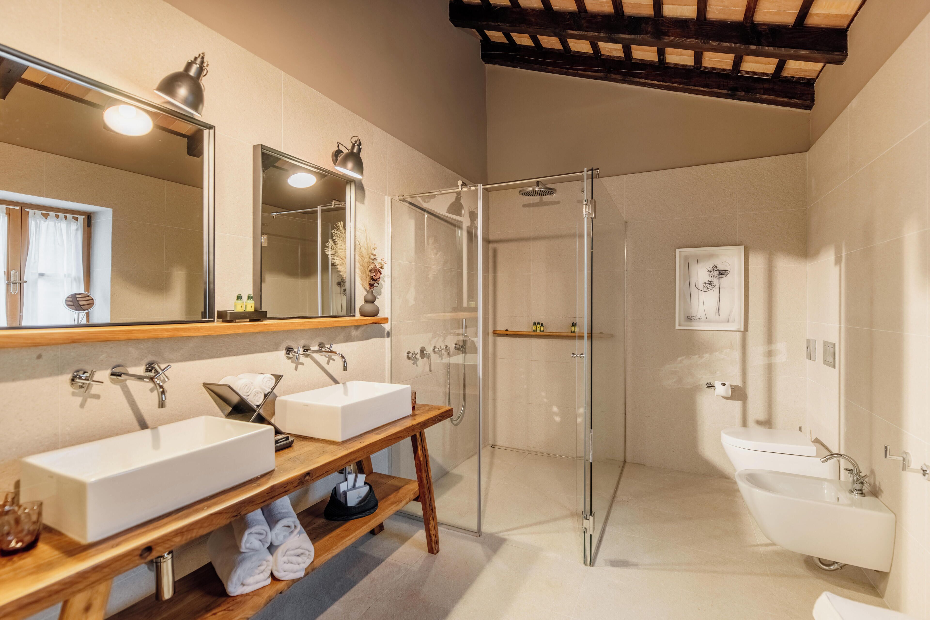 Ein modernes Badezimmer mit zwei Waschbecken, einer Glasdusche und einem Holzwaschtisch.