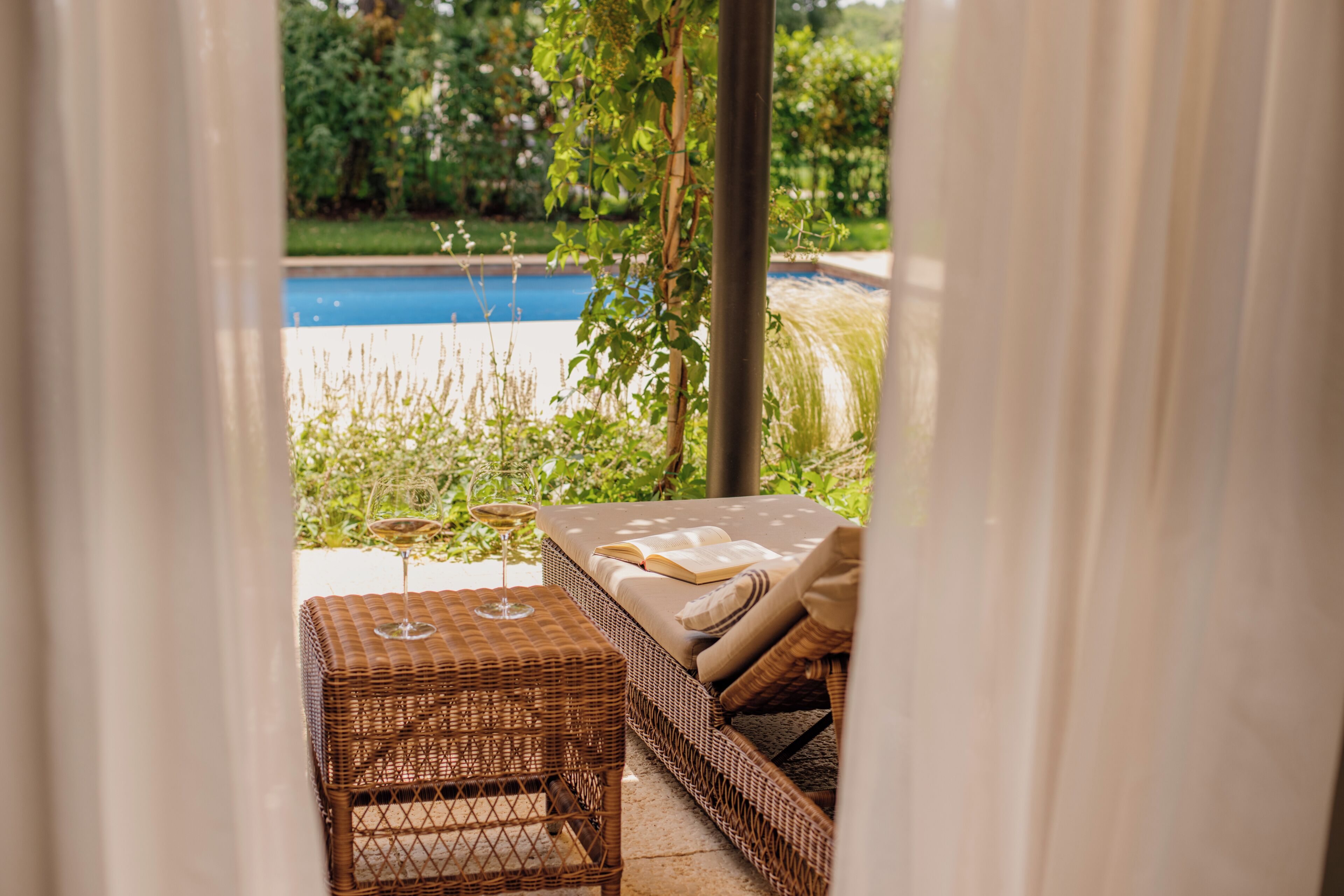 A wicker sofa with a cushion, a glass table, and a wine glass.