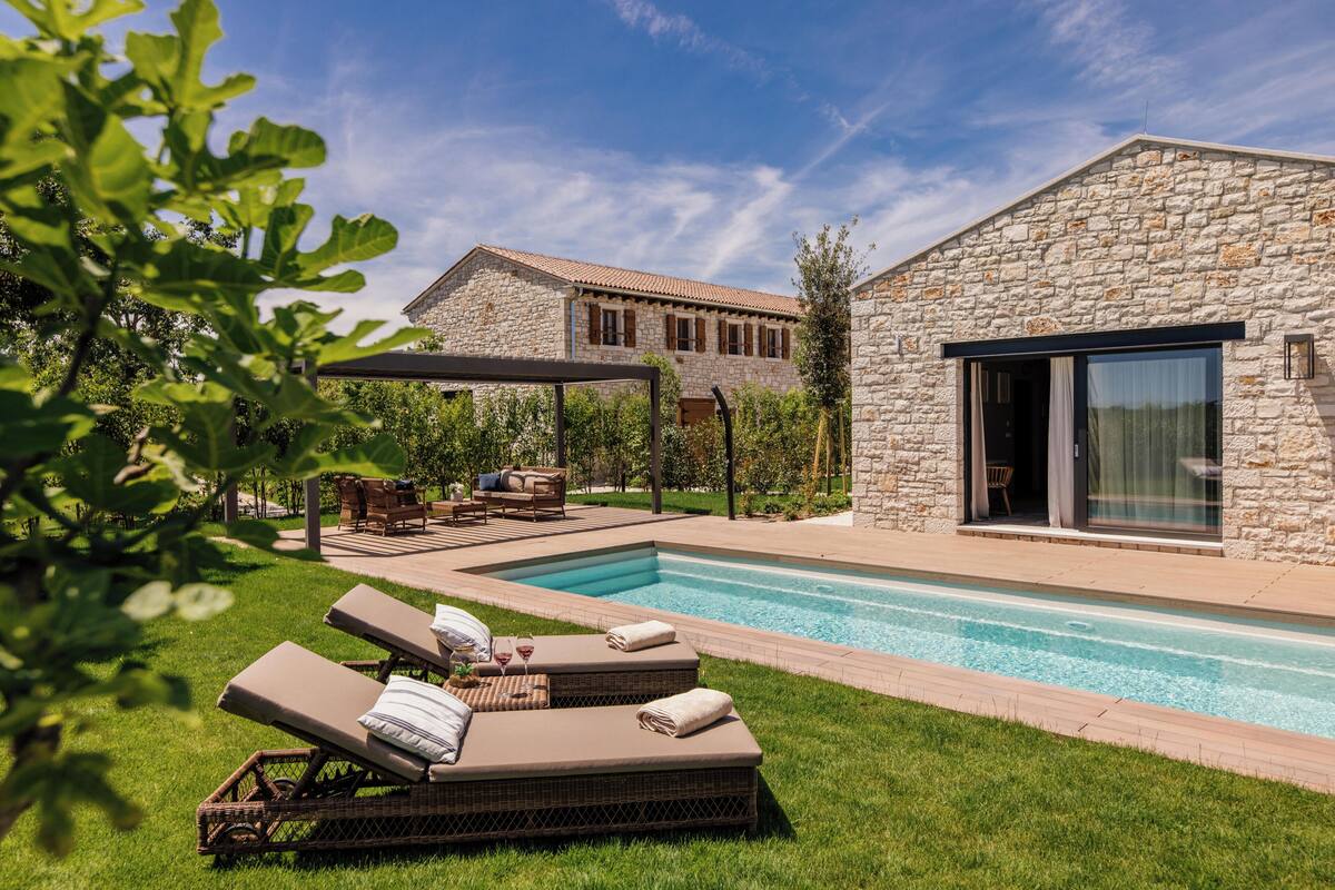 A stone building with a swimming pool, lounge chairs, and a covered patio area.
