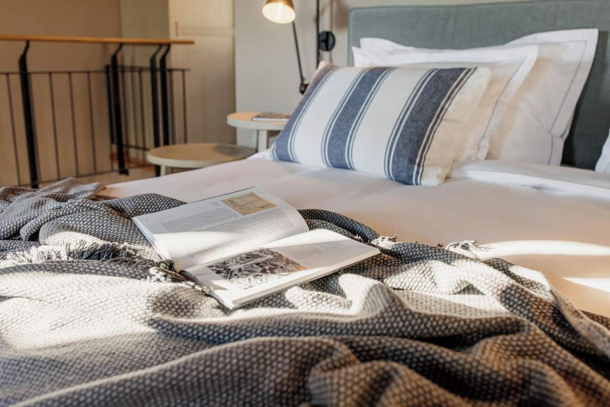 A neatly made bed with a striped pillow, a book, and a blanket.