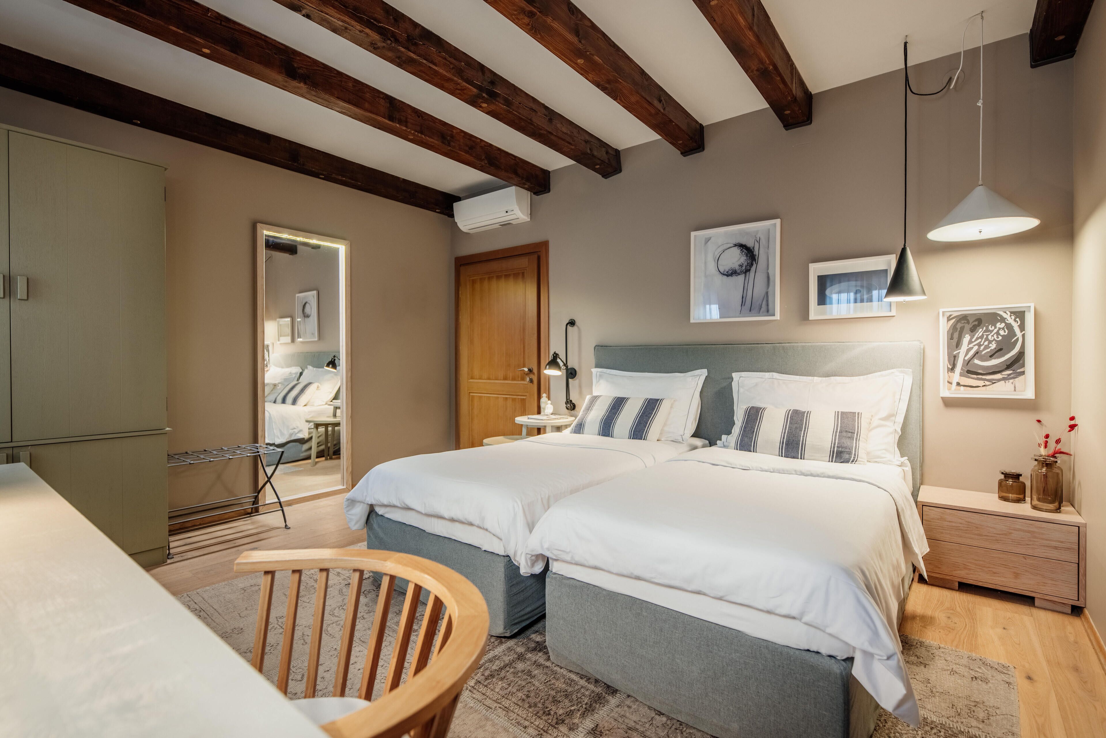 Un dormitorio con dos camas, techo de madera, mesita de noche con lámpara y una obra de arte en la pared.