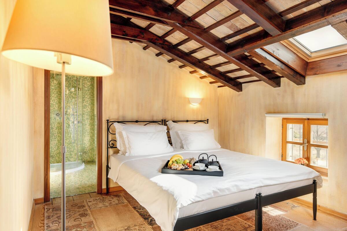 A bedroom with a bed, a tray of fruit, a lamp, a window, and a skylight.