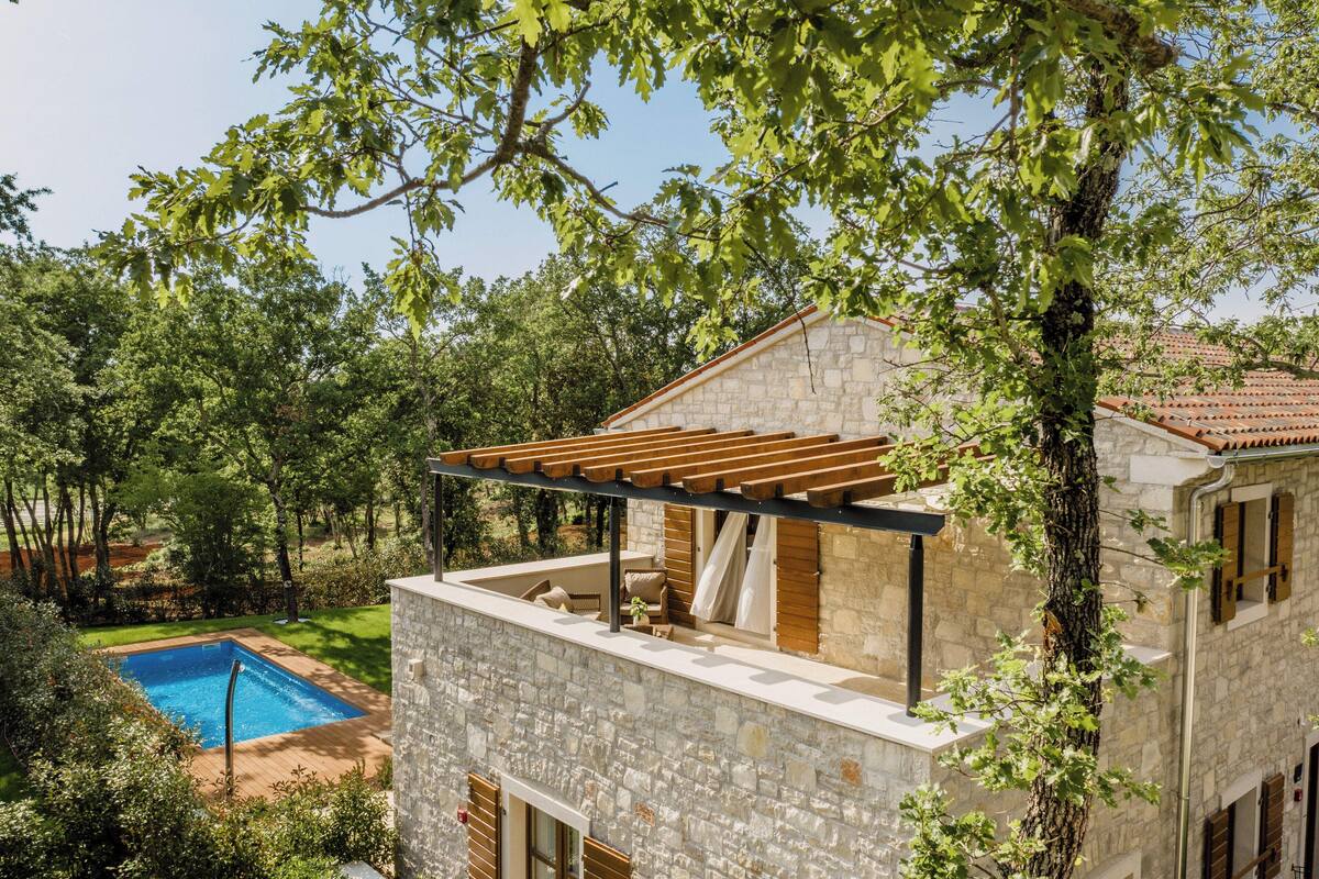 A stone building with a wooden pergola and a swimming pool.