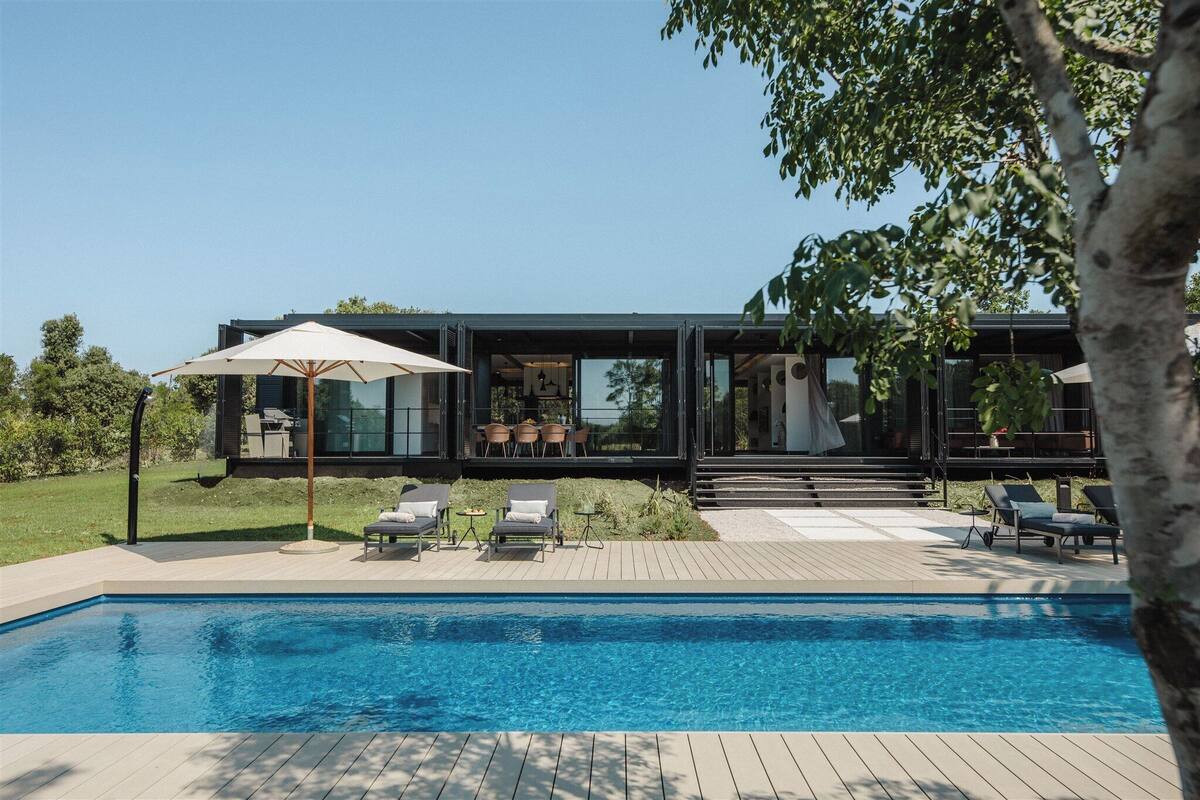 A modern house with a swimming pool, outdoor seating, and a large umbrella.