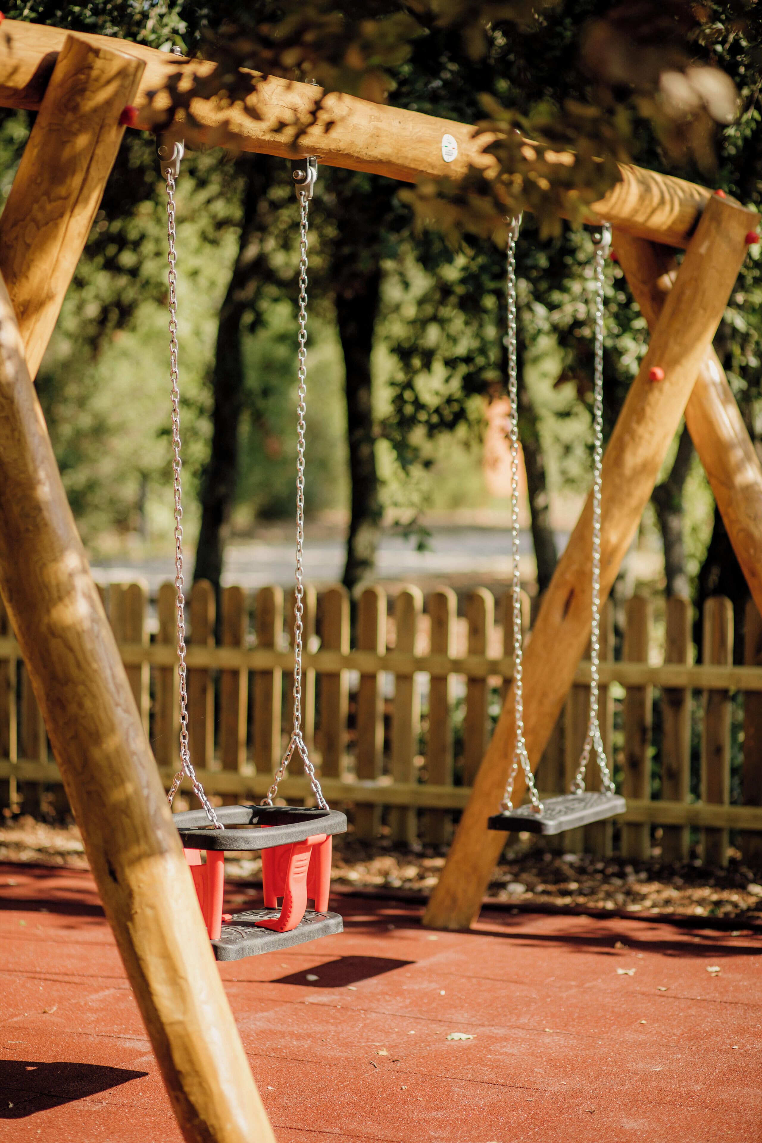A wooden swing set with metal chains and red seats in a park.