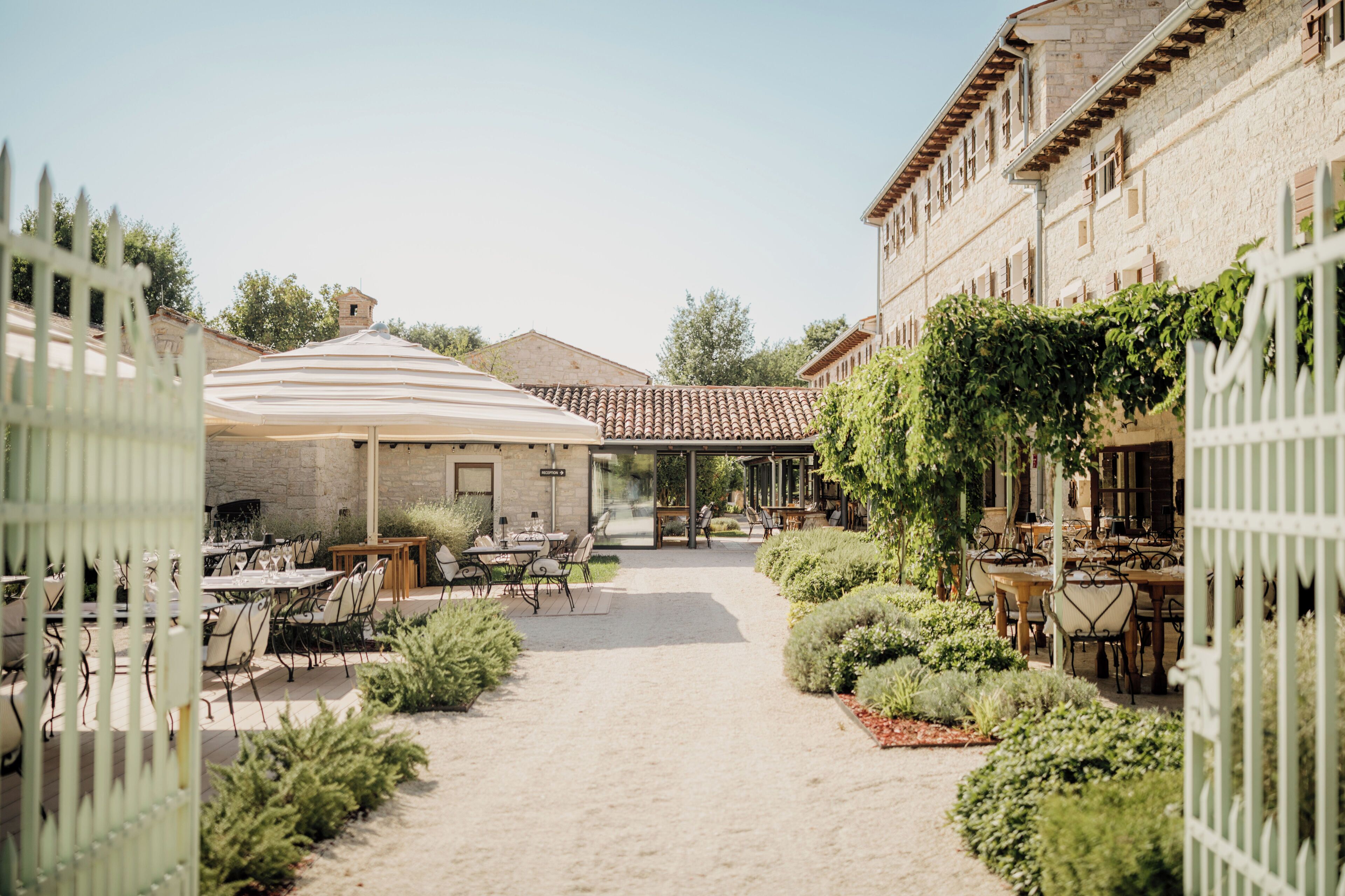 An outdoor dining area with tables and chairs, a covered seating area, and a pathway leading to a building.