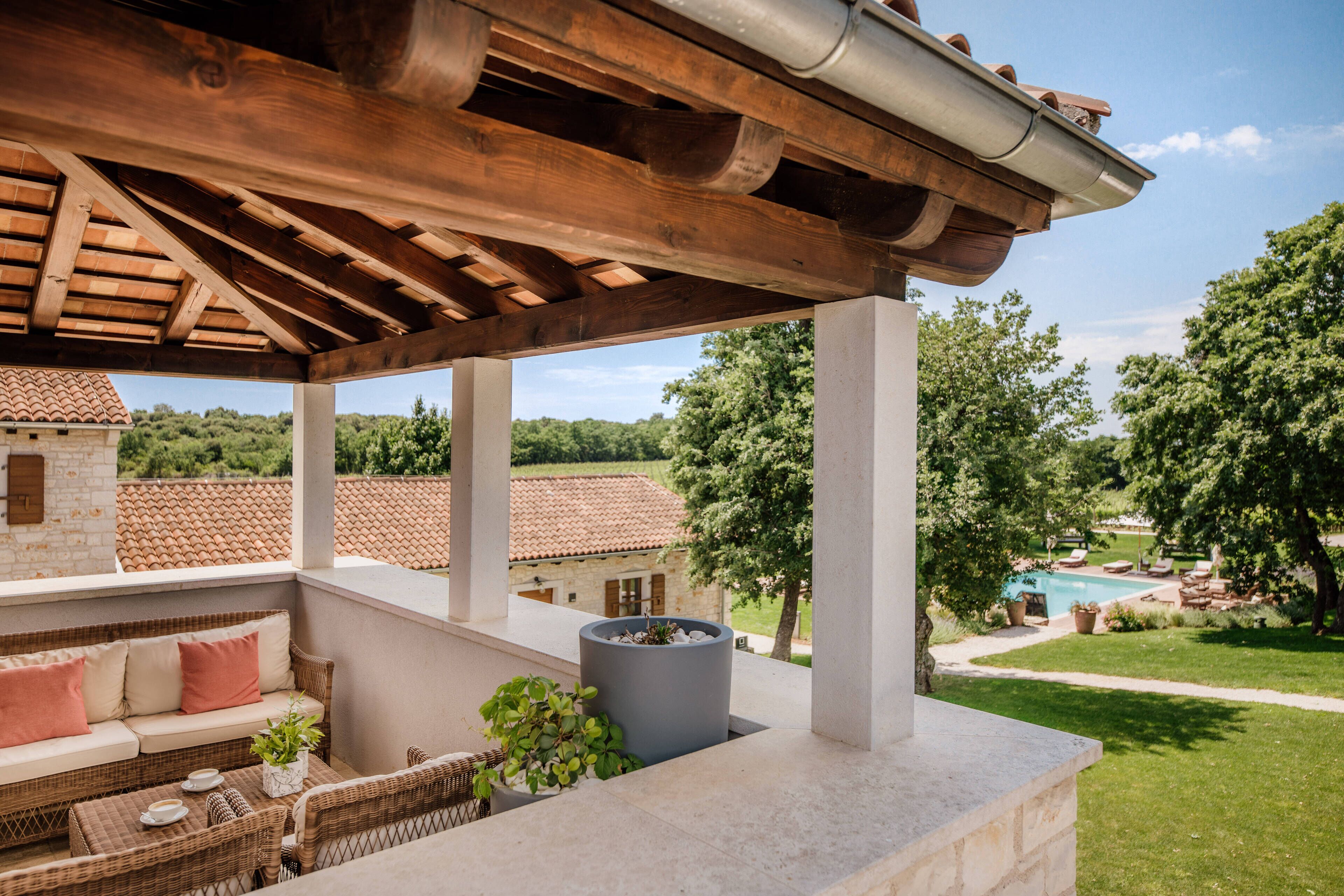 A covered outdoor seating area with a view of a swimming pool and garden.