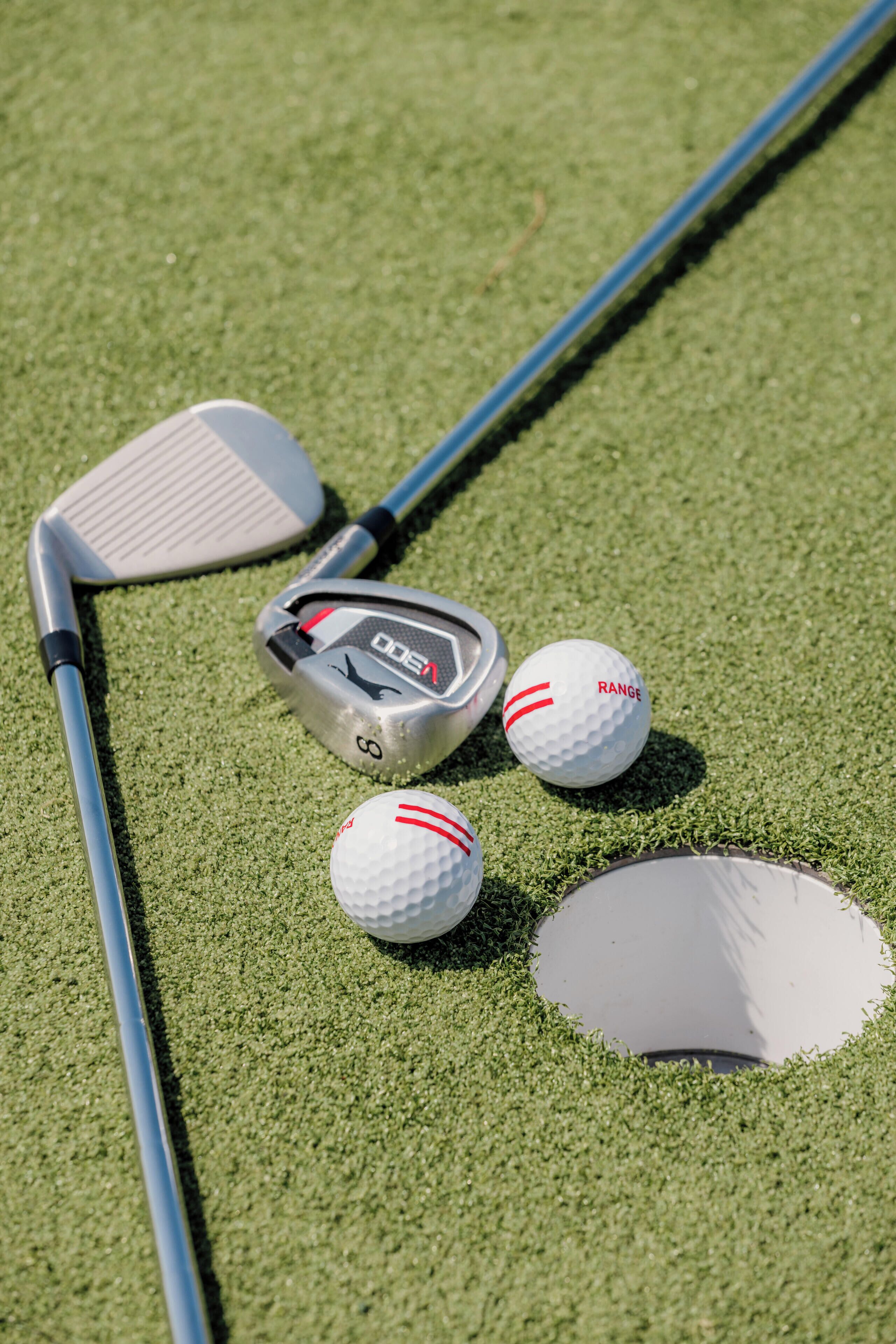 Un club de golf, deux balles de golf et un trou pour le putting sur une surface verte.