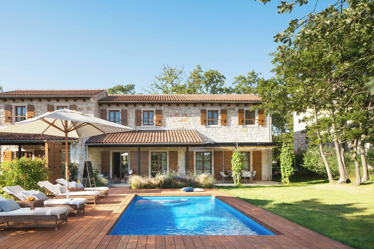 A two-story stone building with a swimming pool, outdoor seating, and a well-maintained lawn.
