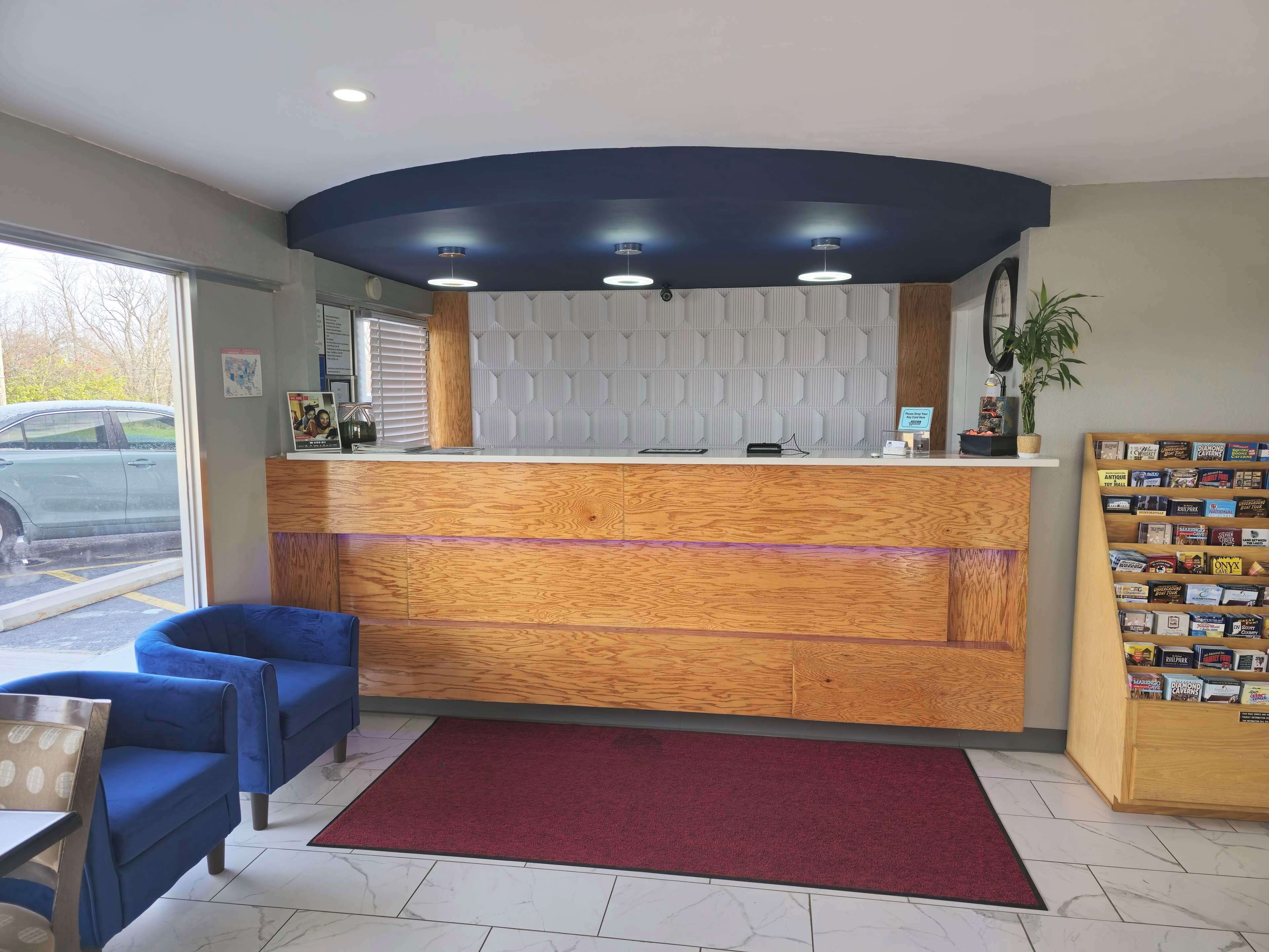 A reception area with a wooden counter, blue chairs, a red carpet, and a bookcase.