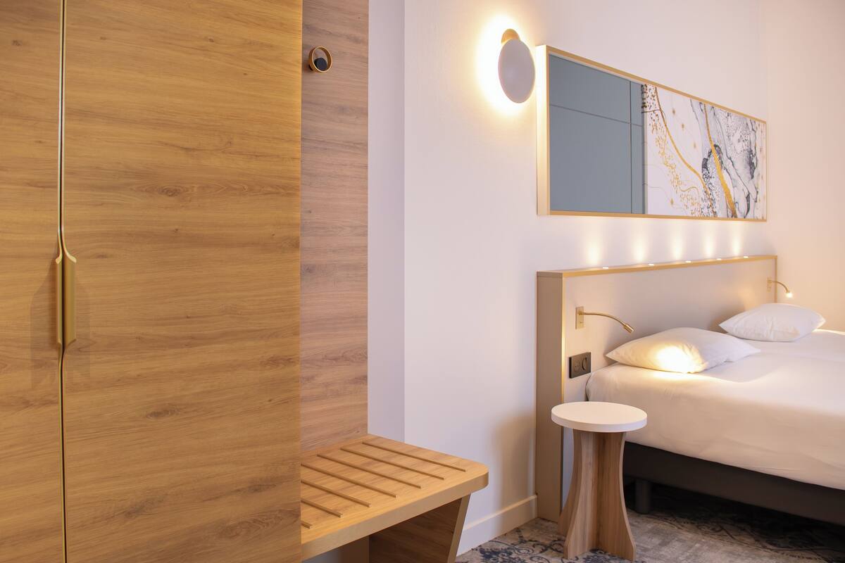 Ein modernes Schlafzimmer mit einem Holzschrank, einem Nachttisch, einem Bett mit weißer Bettwäsche und einem beleuchteten, wandmontierten Spiegel.