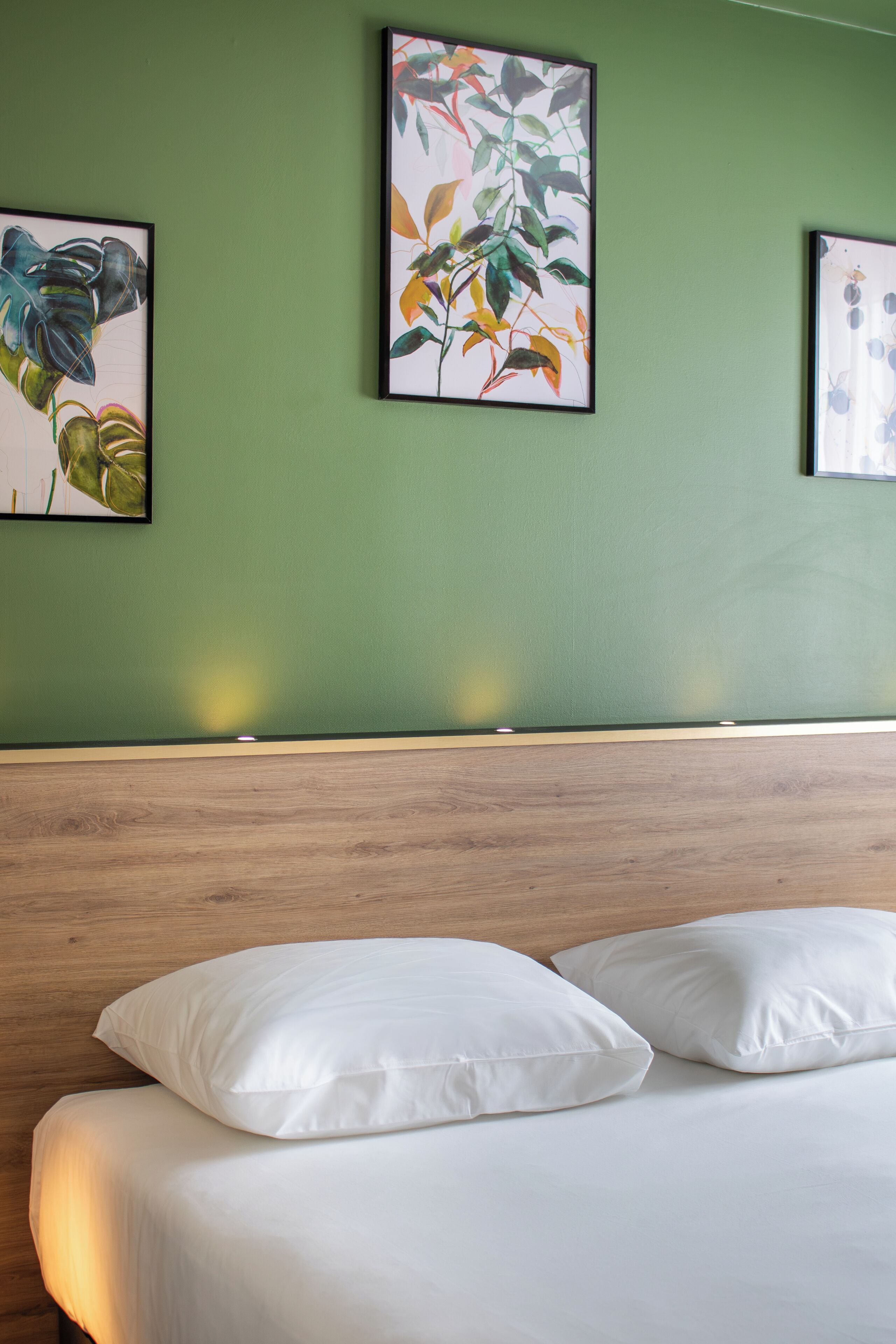 Habitación de hotel con cabecera de madera, cama con ropa blanca y tres cuadros botánicos en la pared.