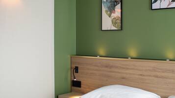 Una habitación de hotel con una cama, una mesita de noche, una lámpara de pared y dos obras de arte enmarcadas.