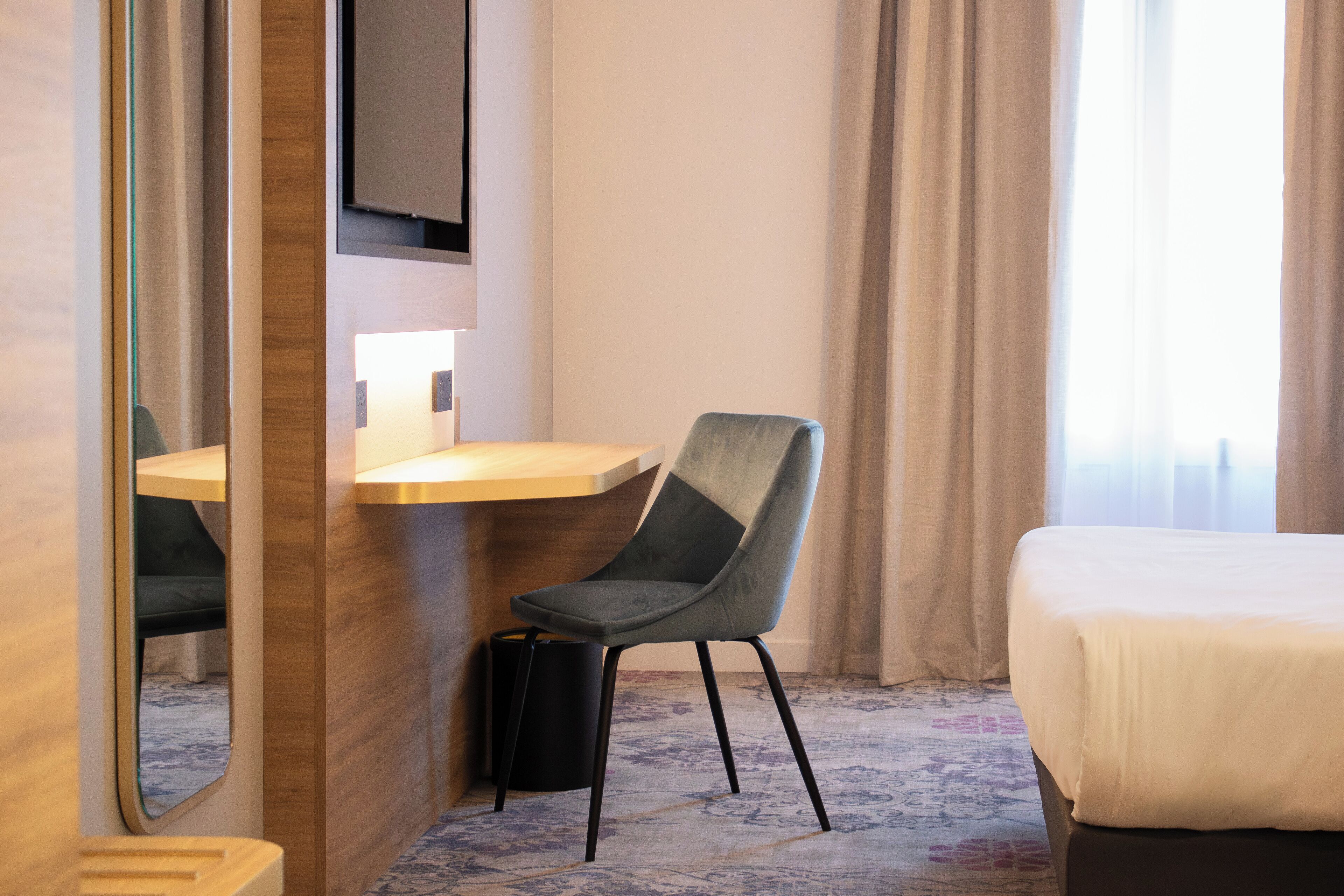 Une chambre d’hôtel équipée d’un lit, d’un bureau, d’une chaise, d’une télévision et d’un miroir.
