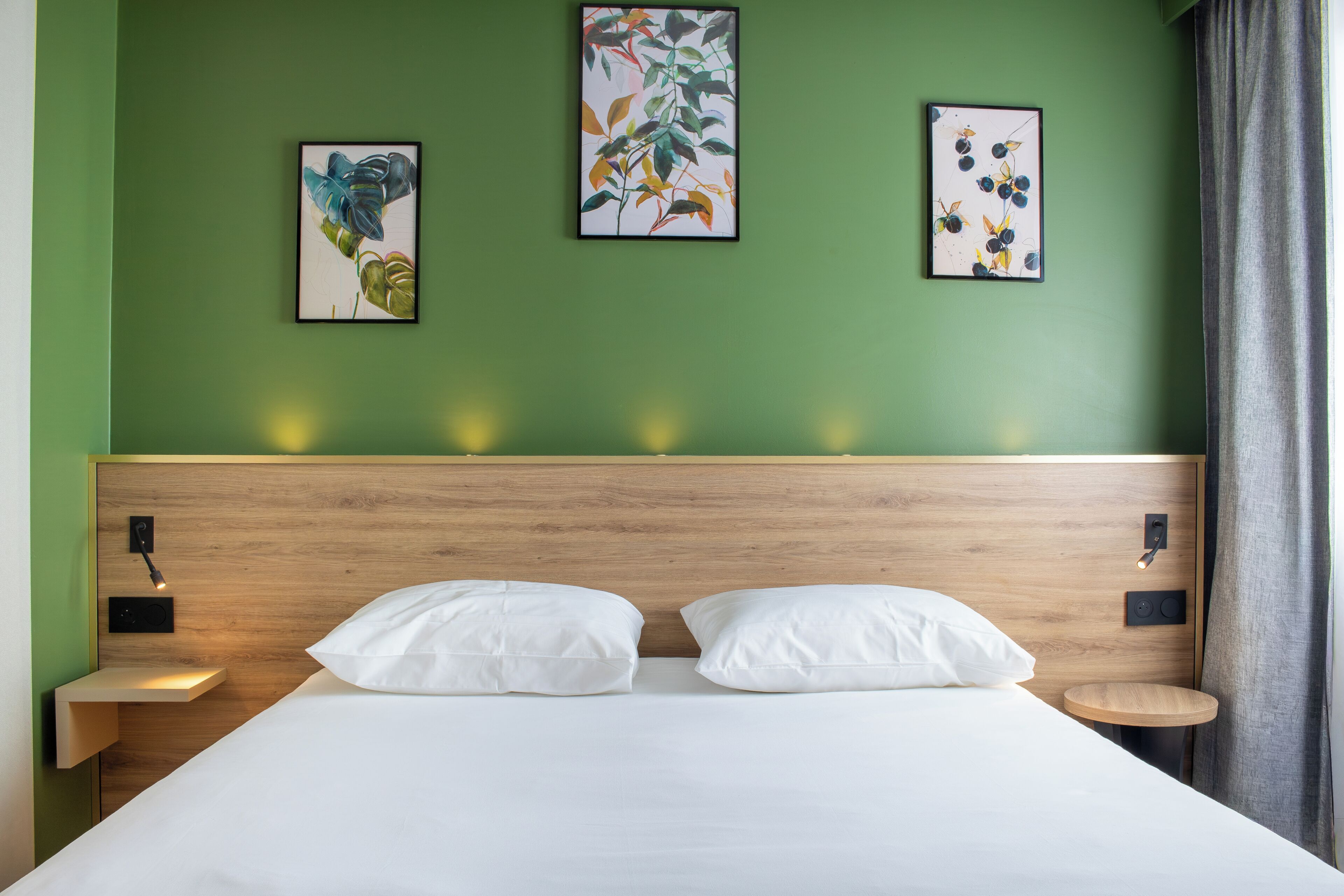 Habitación de hotel con cabecera de madera, dos almohadas blancas y tres cuadros en la pared.