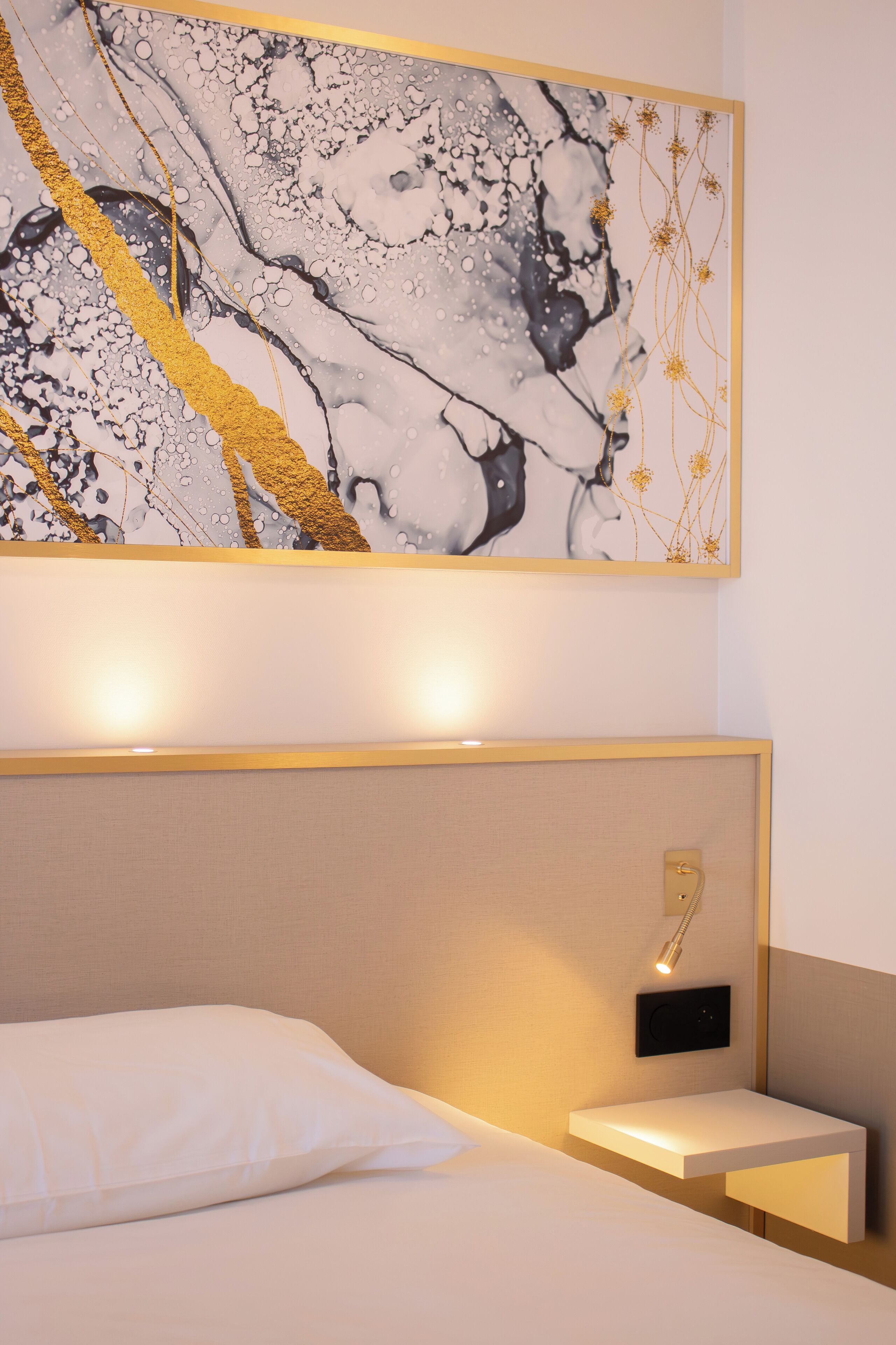A modern hotel room with a large abstract painting, a bedside table with a lamp, and a headboard.